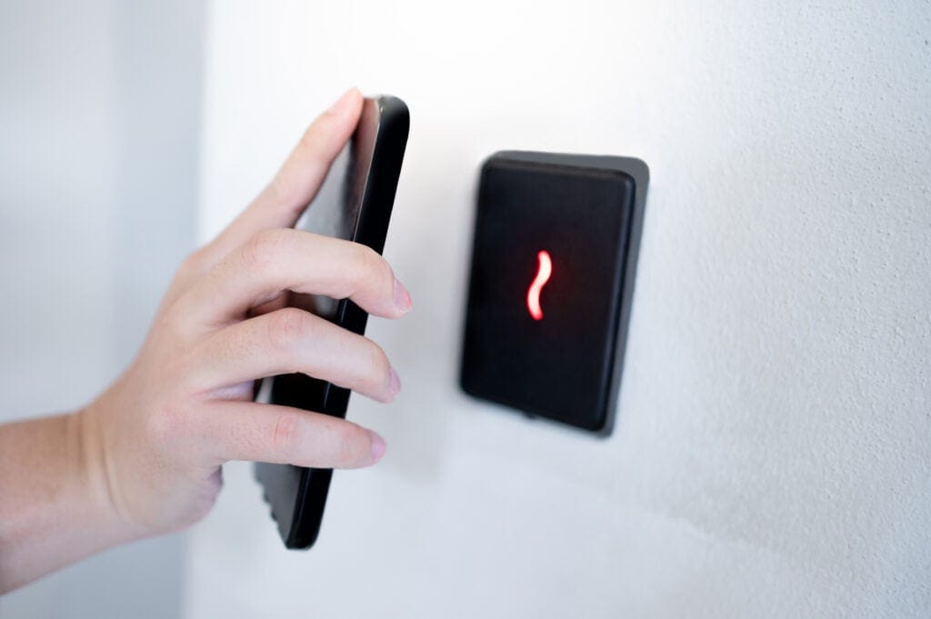 Close-up of a person using a smartphone near a smart switch with red light, demonstrating structured data cabling solutions for home and office.