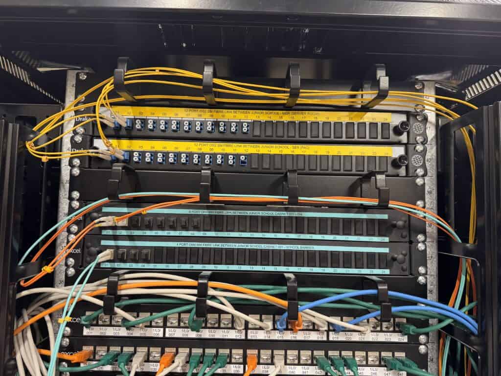 Close-up of labelled OS2 single-mode fibre patch panels linking the junior school equipment room to the school's Main Equipment Rooms