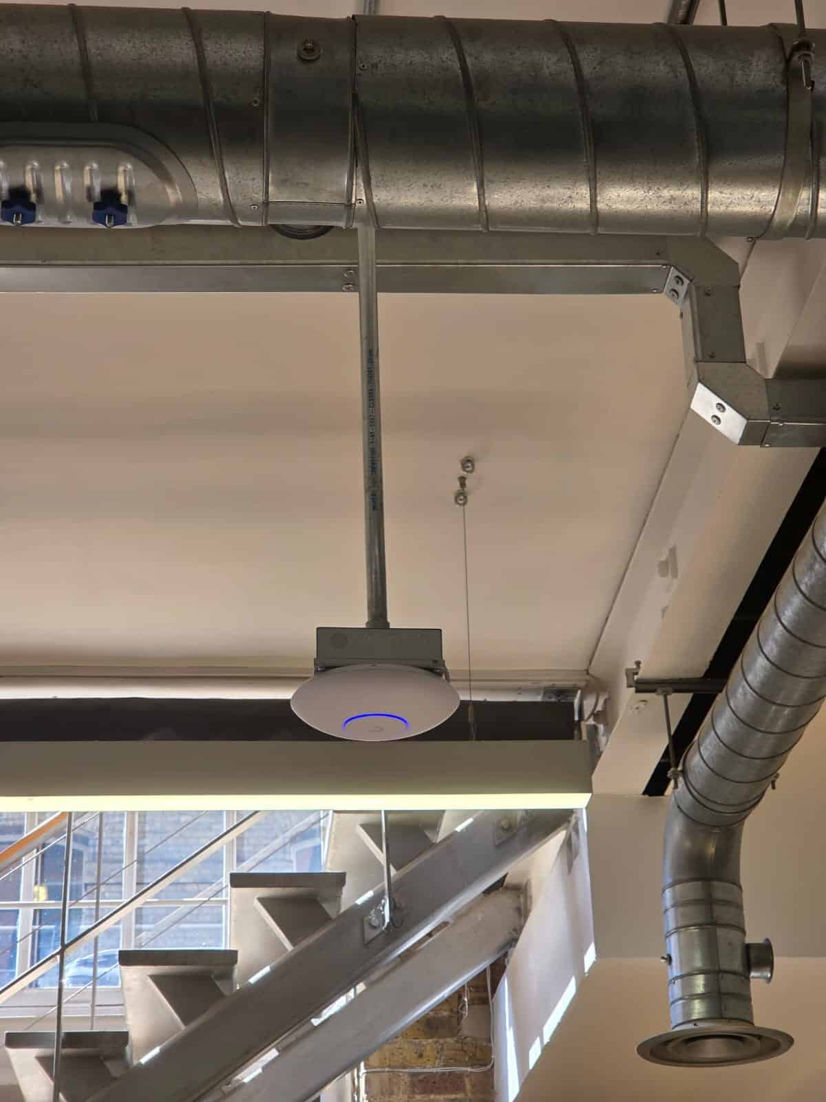 Ubiquiti Wi-Fi 7 access point mounted on the exposed ceiling at Tidraw's Old Street office