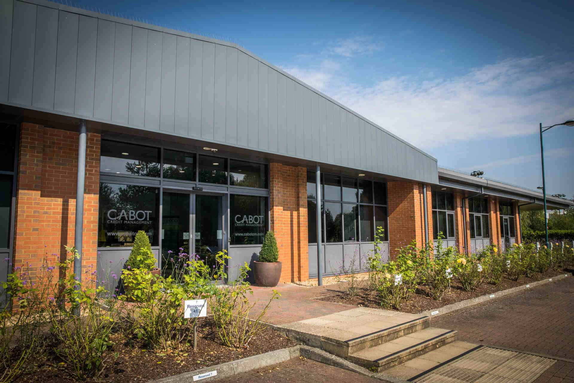 Exterior view of Cabot Financial's Kings Hill campus office building in Kent, glazed facade with visible Cabot Credit Management signage, secured by ACCL's Avigilon CCTV and access control system