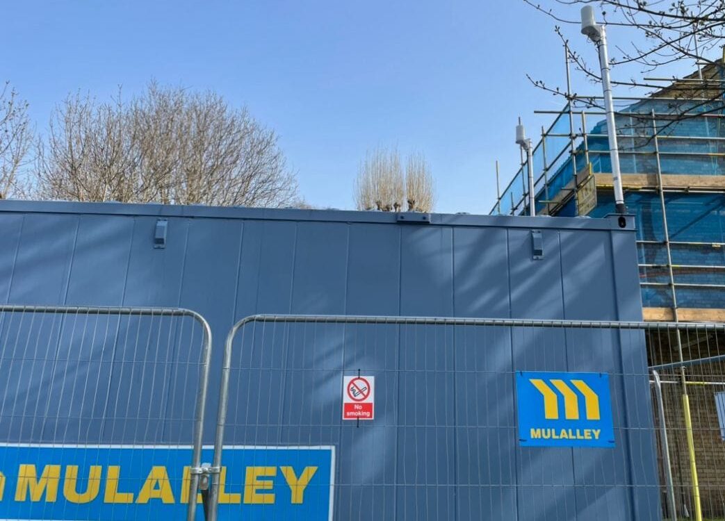 A Mulalley-branded temporary site cabin with ACCL's roof-mounted external antenna and a second antenna visible on the cabin behind, part of the standardised 5G connectivity build.