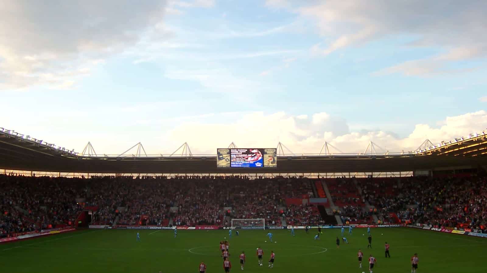Stadium with players on the field and a large screen in the background.